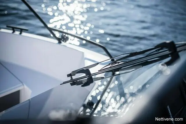Close-up of a boat windshield with wipers, reflecting sunlight on the water, showcasing a sleek nautical design.
